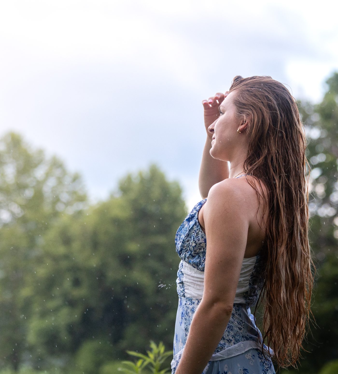Profile portrait looking up and shielding eyes, backlit hair in the rain