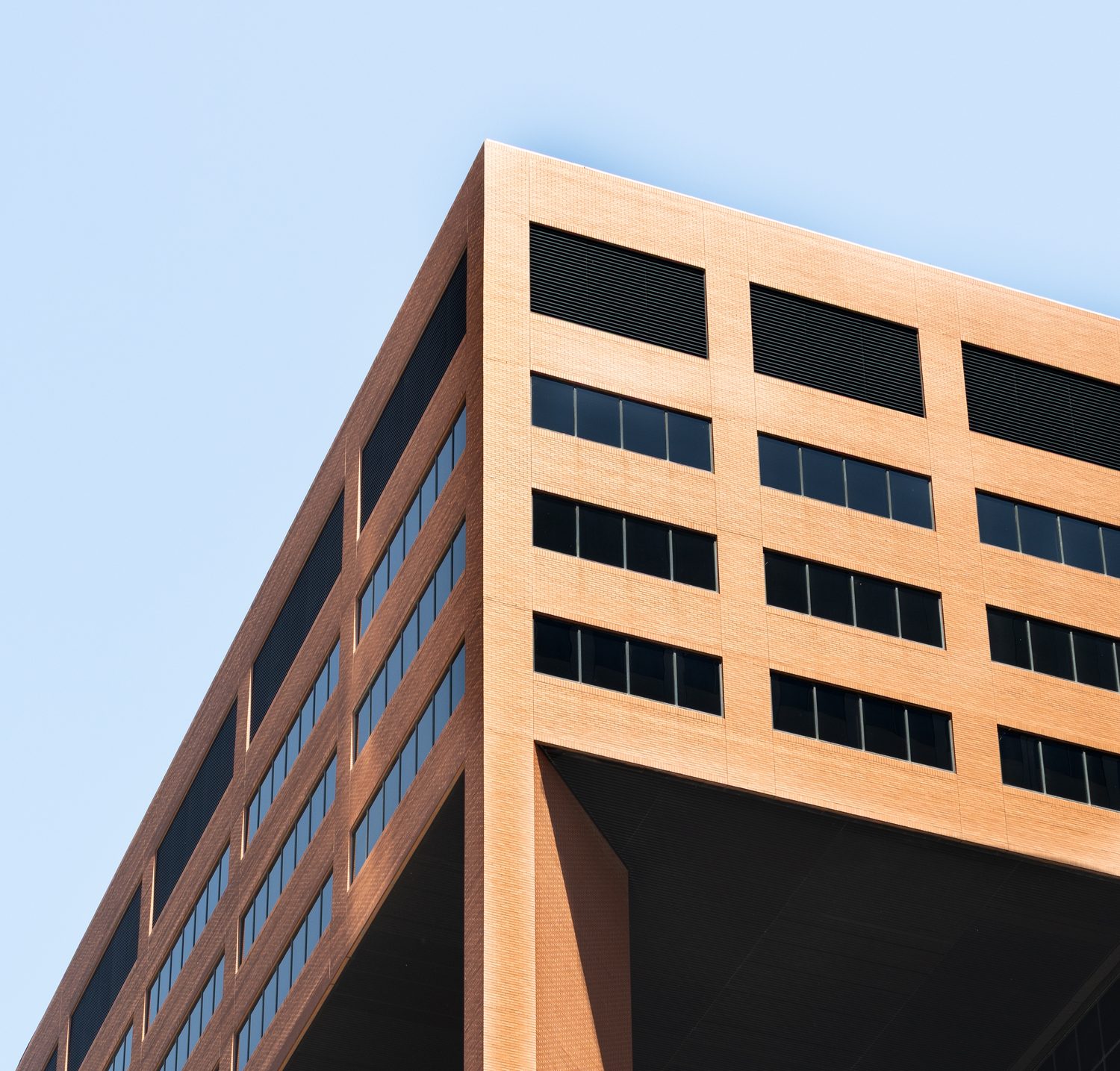 Modern tan brick office tower corner against a clear blue sky