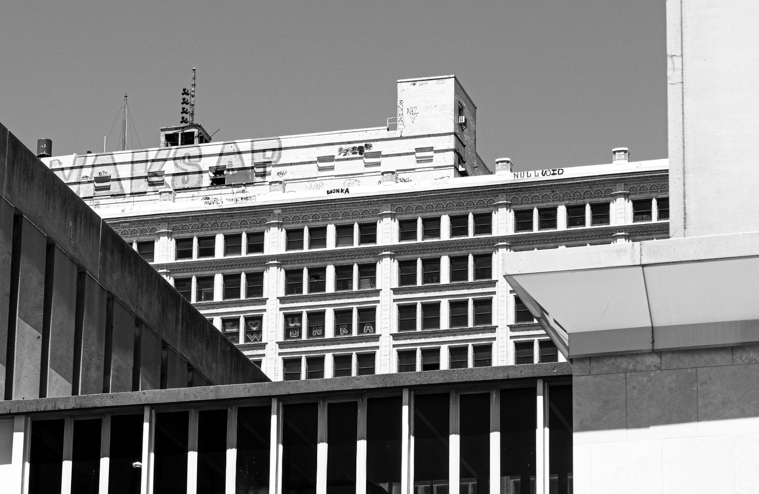 Black and white photo of rooftop graffiti and an ornate cornice on a downtown building