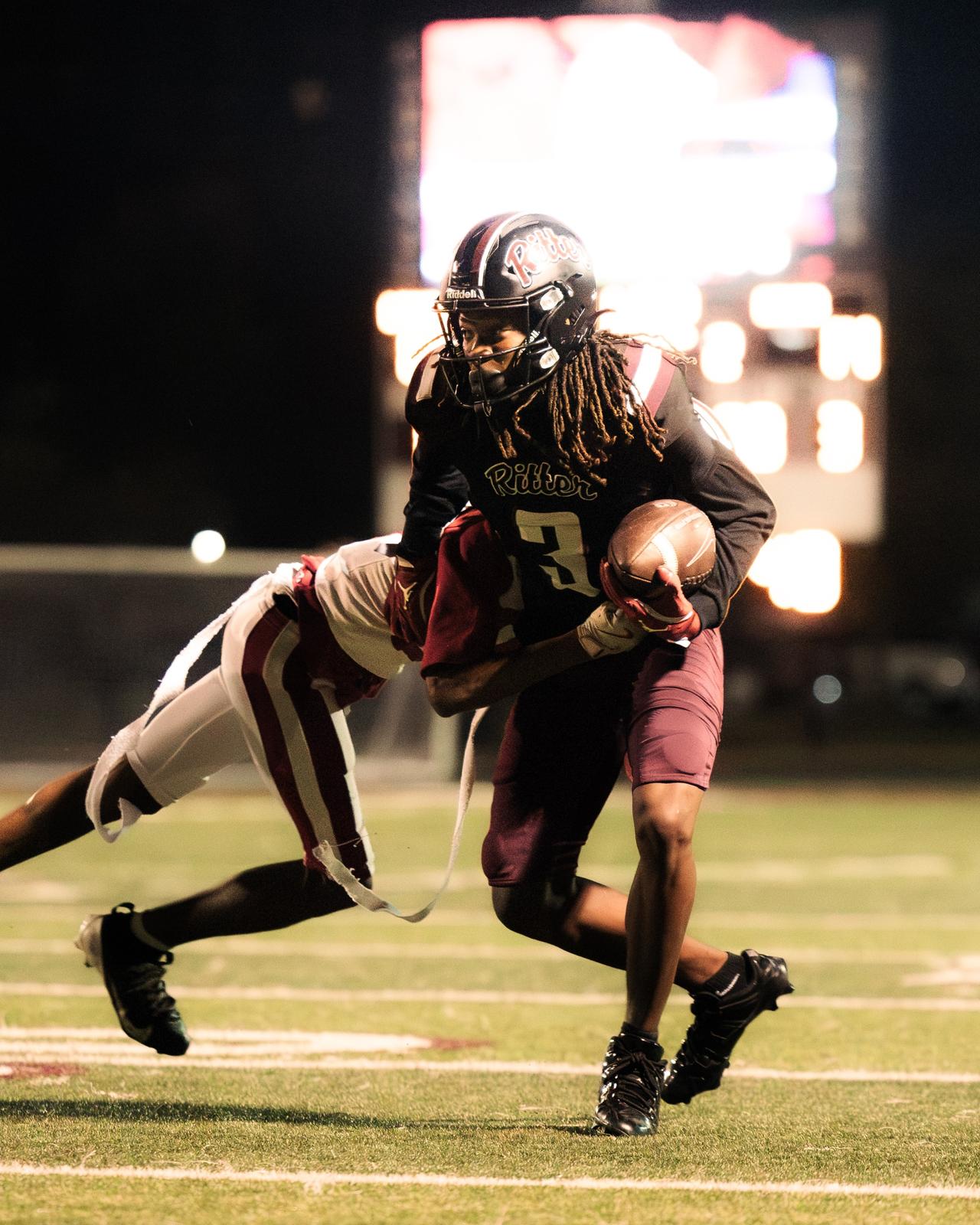 Ball carrier in a dark jersey breaking a tackle at night under stadium lights