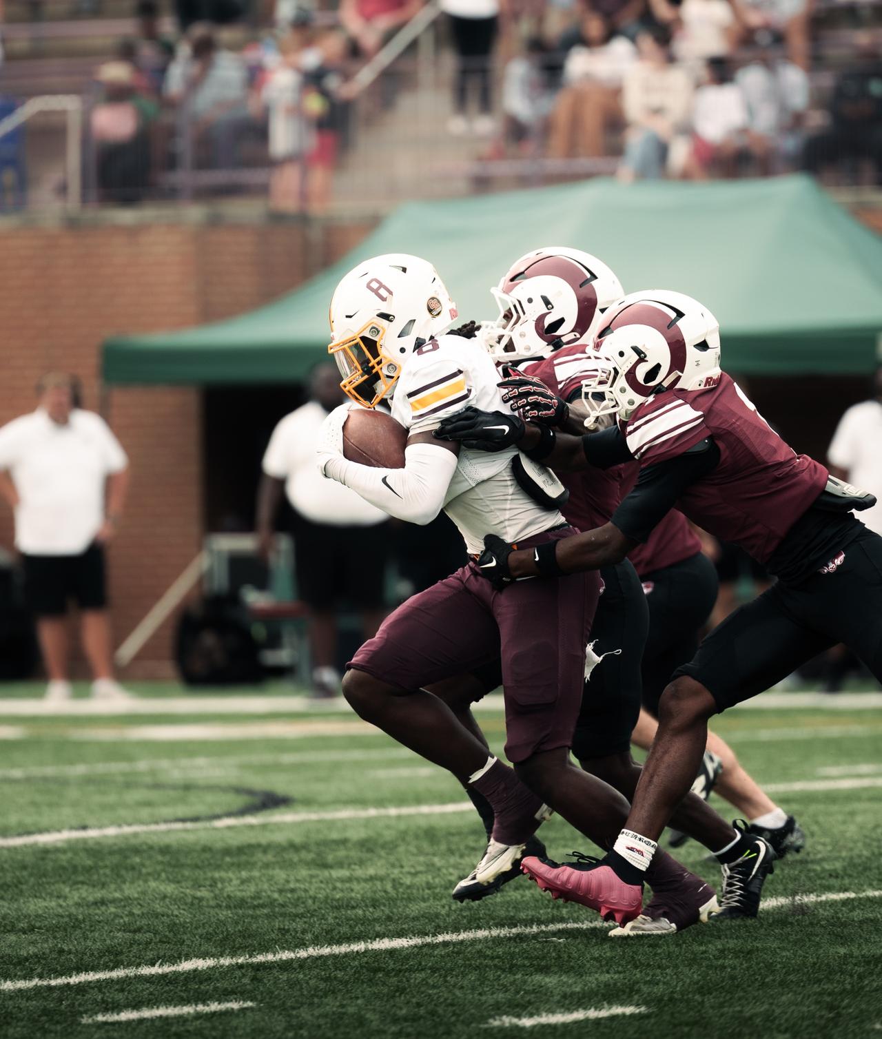 Ball carrier driving through maroon defenders in front of a green tent
