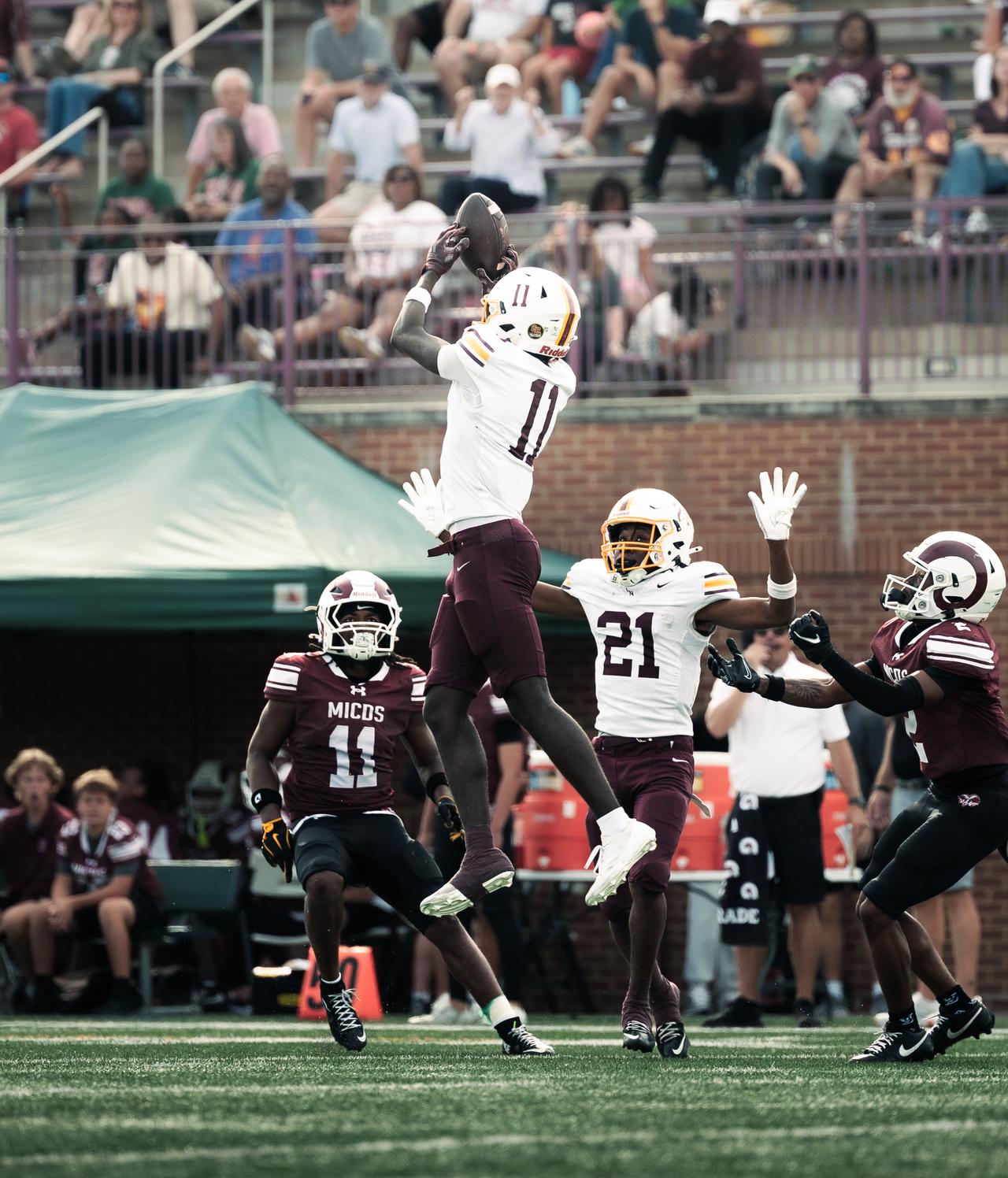 Receiver in white and maroon leaping to catch the ball above three defenders