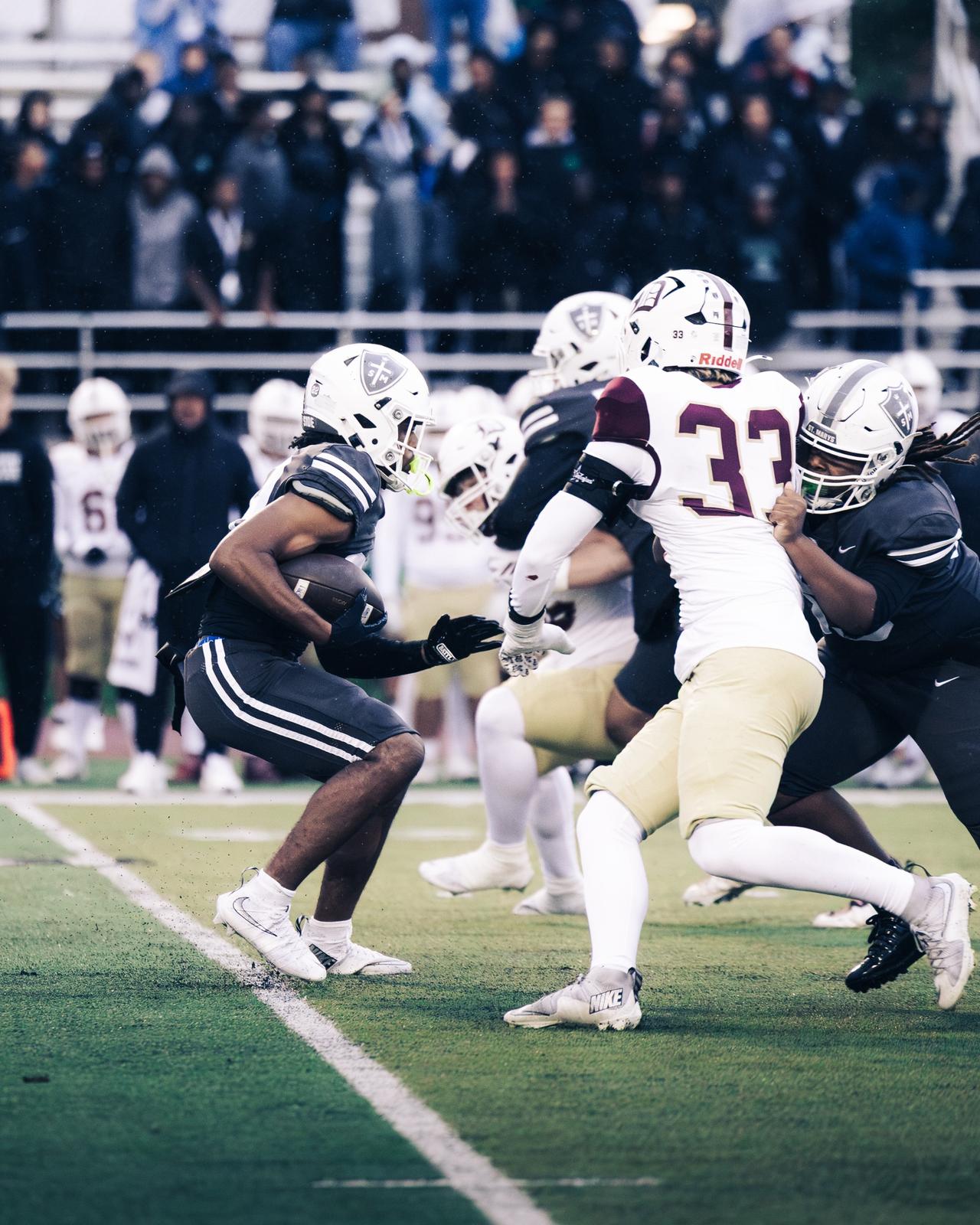St. Mary's ball carrier in the rain facing a defender in a white and maroon jersey