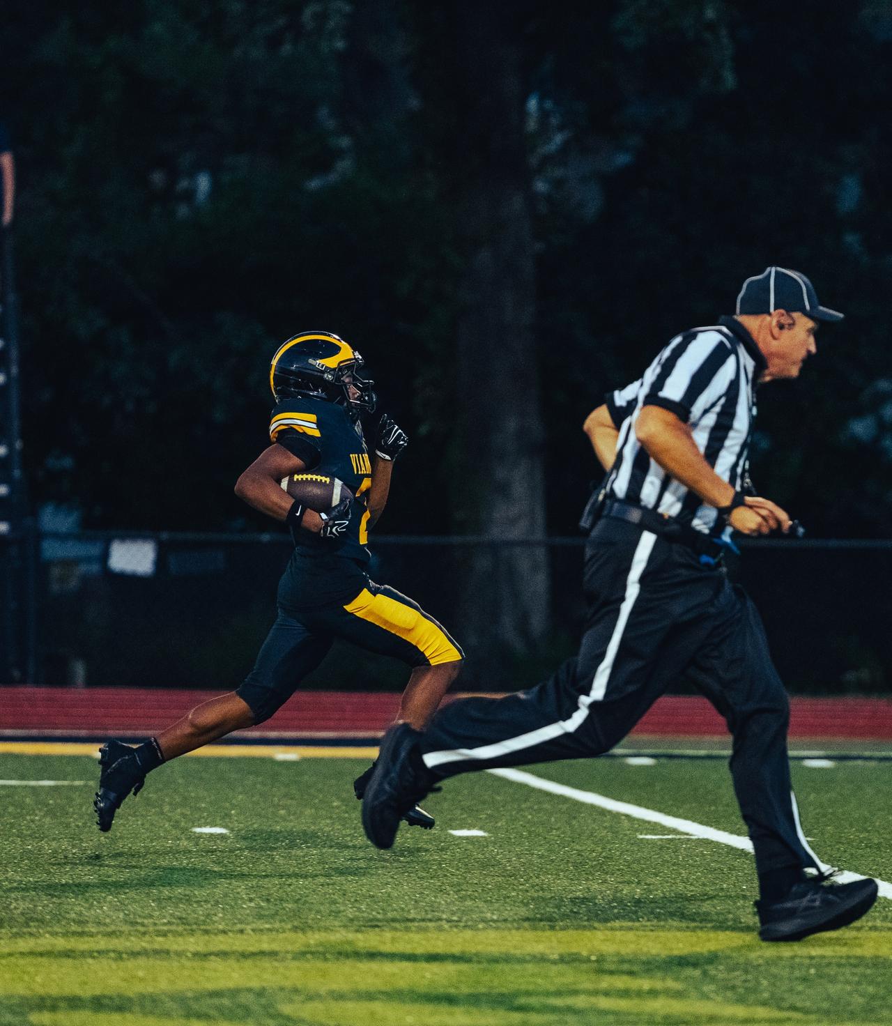 Vianney ball carrier sprinting down the sideline past a running referee