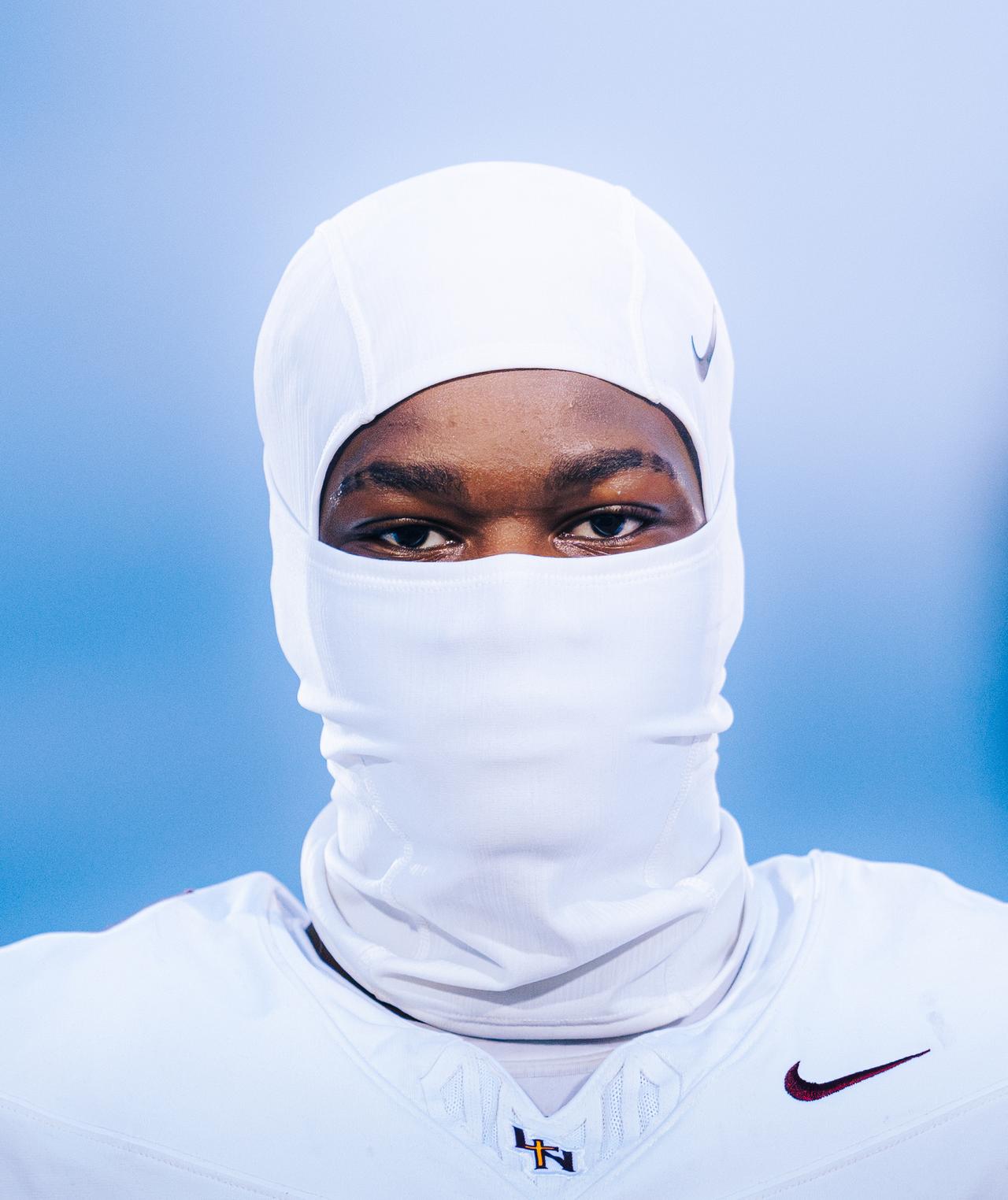 Player in a white balaclava looking straight at the camera against a blue background